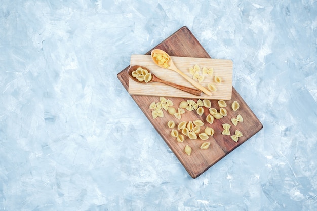 Set of wood piece and raw pasta in wooden spoons on grungy and cutting board background. top view.