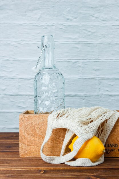 Набор деревянного ящика, пустой бутылки и лимона на деревянной и белой поверхности. вид сбоку. место для текста