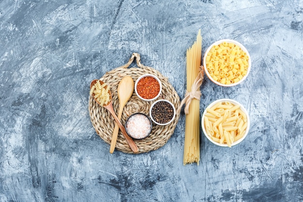 Set of wooden spoons, spices and assorted pasta in bowls on grey plaster