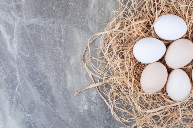 Several chicken fresh eggs on hay on marble background. High quality photo