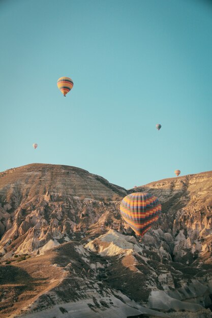 Several colorful hot air balloons floating above mountains