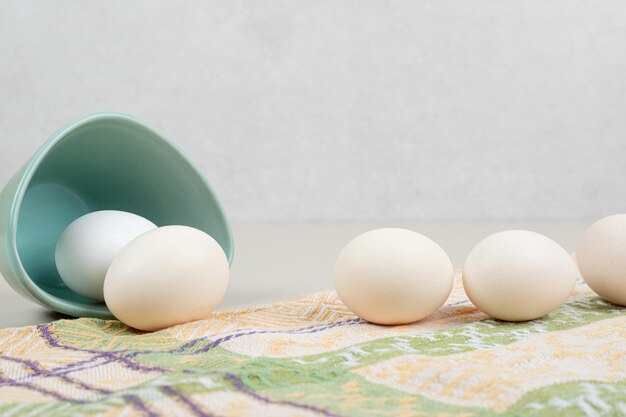 Several fresh chicken white eggs in blue plate on tablecloth.