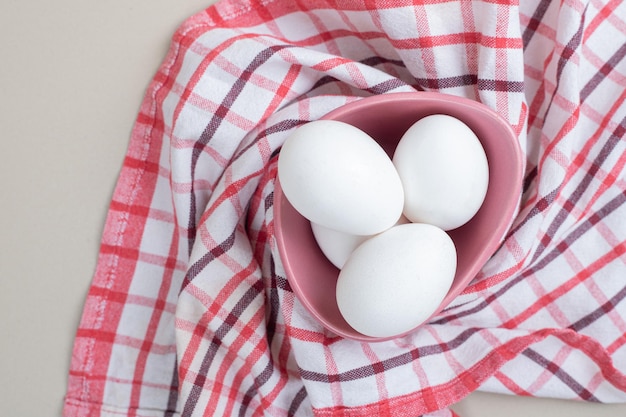 Several fresh chicken white eggs in pink plate on tablecloth.