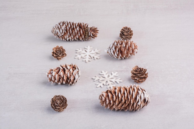 Several pine cones and snowflakes on white table.