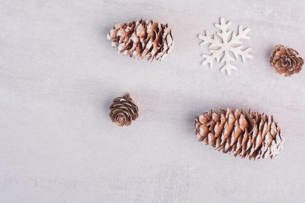 Несколько сосновых шишек и снежинок на белом столе.