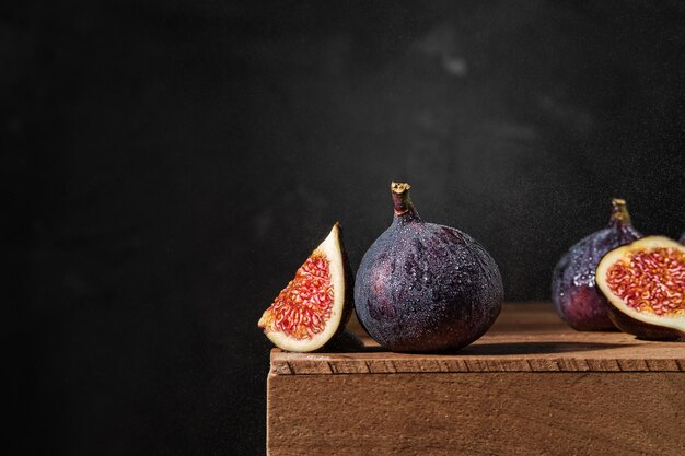 Several ripe figs on a wooden box in raindrops. Close-up, selective focus