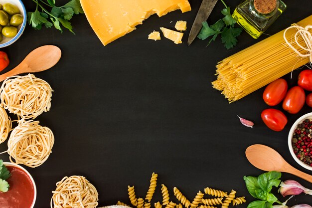 Several types of dry pasta with vegetables and herbs on black background