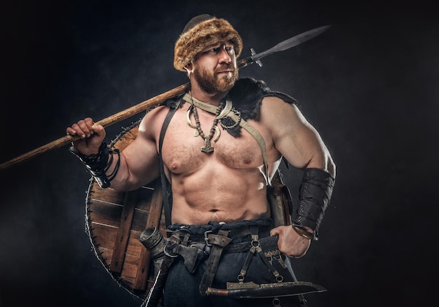 Severe barbarian in warrior clothes, posing on a dark background.