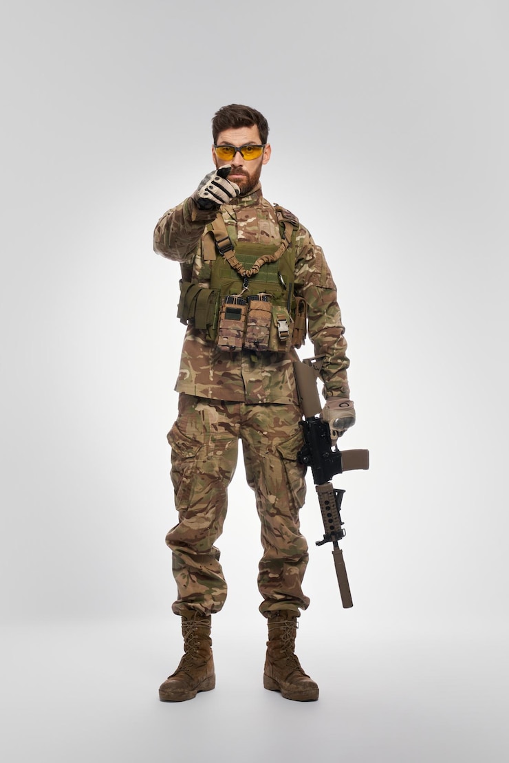 Free Photo severe male soldier with rifle pointing to camera with forefinger indoors front view of force