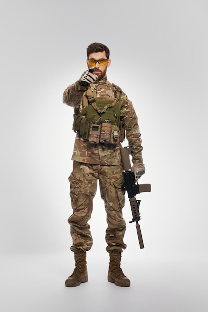 Severe male soldier with rifle pointing to camera with forefinger indoors front view of force