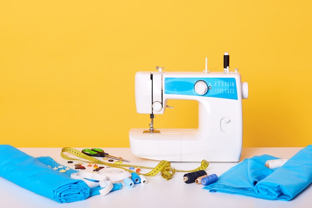 sewing equipments, sewing machine, tap measure, scissors, pieces of cloth, needles, thread isolated on yellow. different tools in sewing workshop,