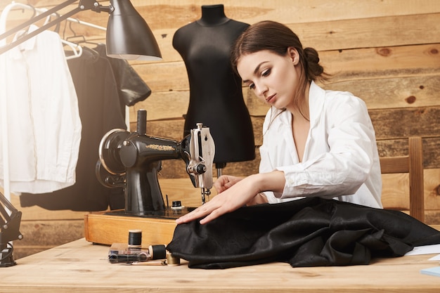 Шить это не просто работа, это талант. Креативный дизайнер, работающий со швейной машиной под своей новой линией одежды, сосредоточенный и прикладывающий усилия, чтобы она выглядела великолепно, находясь в своей собственной мастерской
