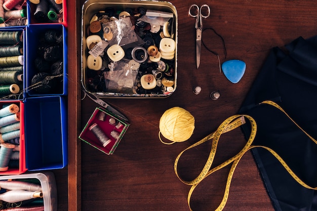 Free photo sewing thread spools; buttons; wool ball; measuring tape; chalk; fabric and scissor on wooden table