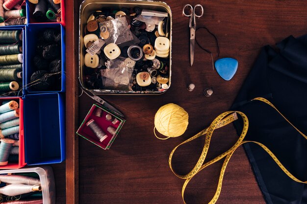 Sewing thread spools; buttons; wool ball; measuring tape; chalk; fabric and scissor on wooden table