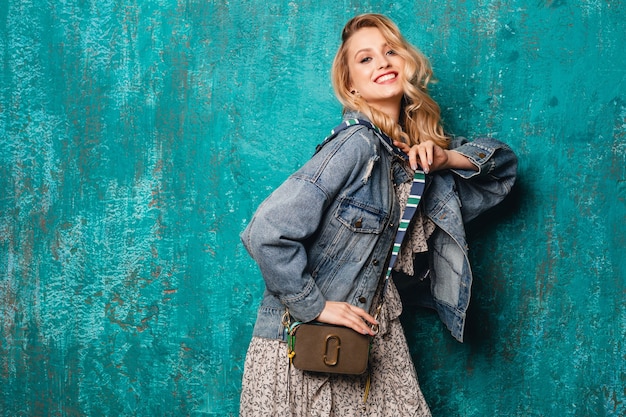 Sexy attractive stylish blonde woman in jeans and oversize jacket walking against vintage green wall in street