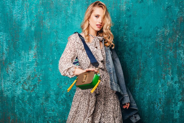 Sexy attractive stylish blonde woman in jeans and oversize jacket walking against vintage green wall in street