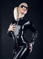 Free photo sexy blond female in sunglasses and in latex black costume isolated on dark background.