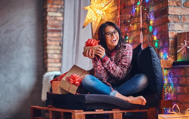 クリスマスの装飾が施された部屋のソファでポーズをとるジーンズと赤いセーターに身を包んだ裸の足でセクシーなブルネットの女性。