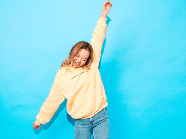 Sexy carefree woman posing near blue wall. Positive model having fun.Raising her hands and shows tongue