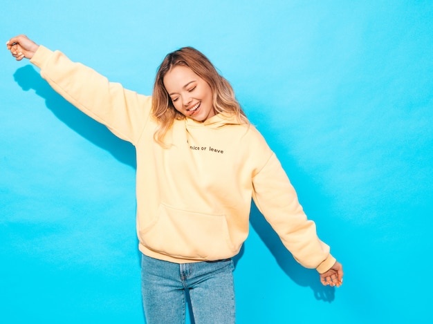 Sexy carefree woman posing near blue wall. Positive model having fun.Raising her hands