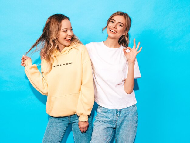 Sexy carefree women posing near blue wall. Positive models having fun.Shows tongue and ok sign