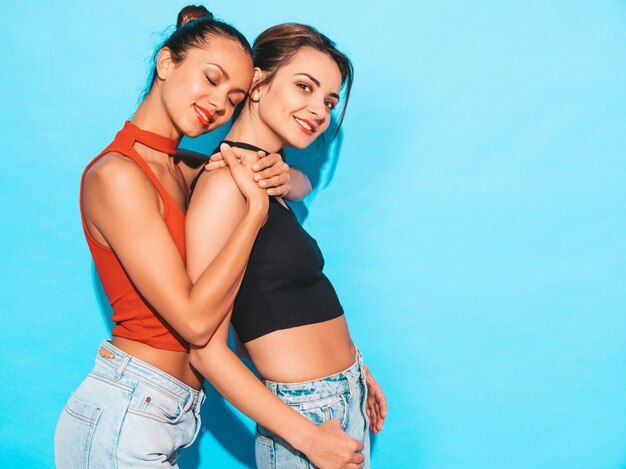 Sexy carefree women posing near blue wall in studio.Positive models having fun.Hugging