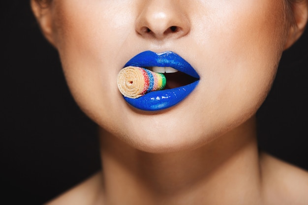 Free photo sexy colorful lips holding sweeties with teeth. over grey wall