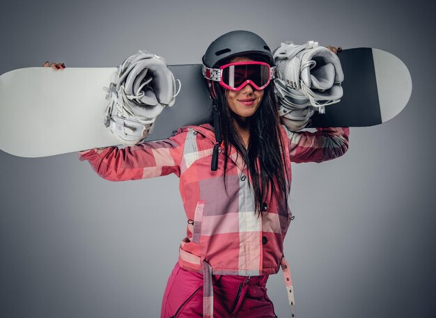 Sexy female in ski costume posing with snowboard in a studio on grey background.