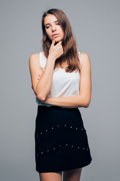 Сексуальная девушка в современном платье моды позирует в студии держит руку на подбородке, изолированные на белом фоне