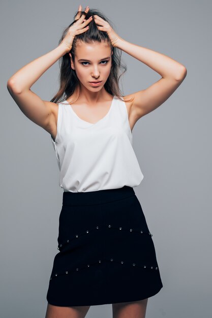 Sexy girl in fashion modern look is posing in studio holds her arms on hair isolated on white background