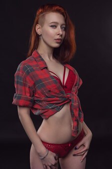 어두운 배경에 아름다운 빨간 속옷과 단추가 없는 셔츠를 입은 섹시한 여자