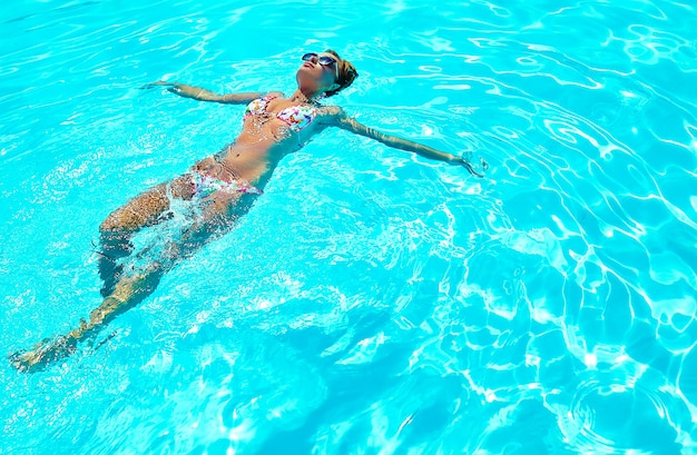 背中に泳ぐカラフルな水着で黒髪のセクシーなホット美少女モデル