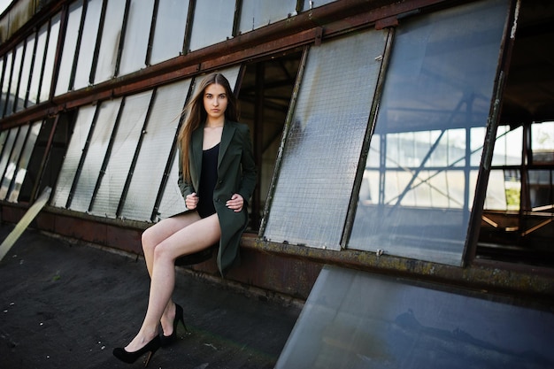 Sexy model girl wit long legs at black lingerie outfit body swimsuit combidress and jacket posed at the roof of abadoned industrial place with windows