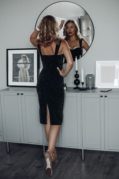 Free photo sexy posh woman in black dress looking in mirror.