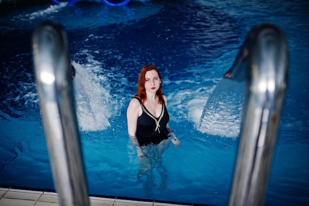 아쿠아 파크의 수영장에서 휴식을 취하는 검은 수영복에 섹시한 빨간 머리 소녀