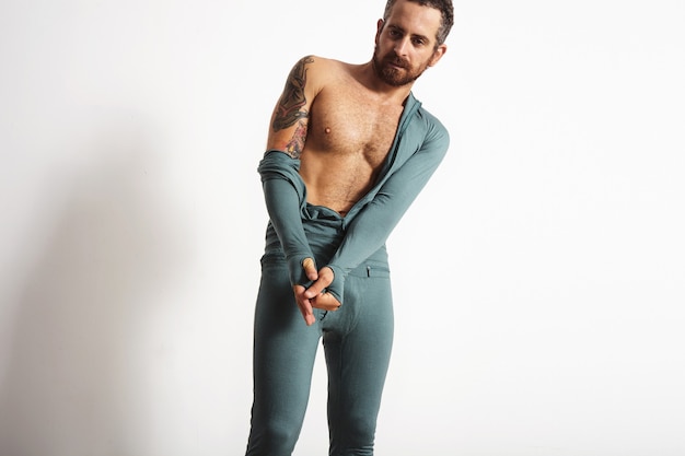 Sexy ripped bearded athlete with tattoo dressing off his baselayer thermal wear, isolated on white