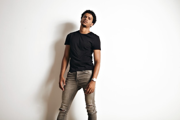 Sexy sensual gloomy looking African American model in a blank black t-shirt and skinny jeans on white wall