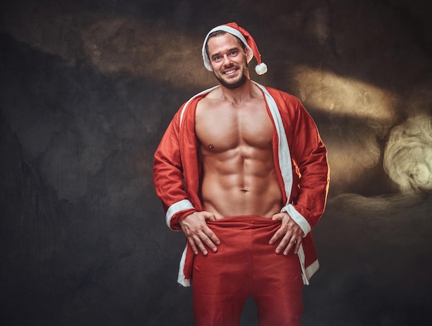 Sexy shirtless Santa in traditional red costume is posing at photo studio.