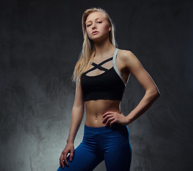 Sexy slim blonde girl in a sportswear posing in a studio. Isolated on a dark background.