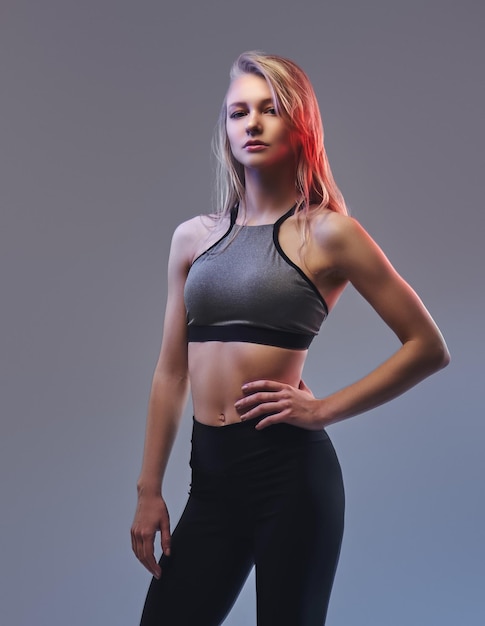 Free photo sexy slim blonde girl in a sportswear posing in a studio. isolated on a gray background.