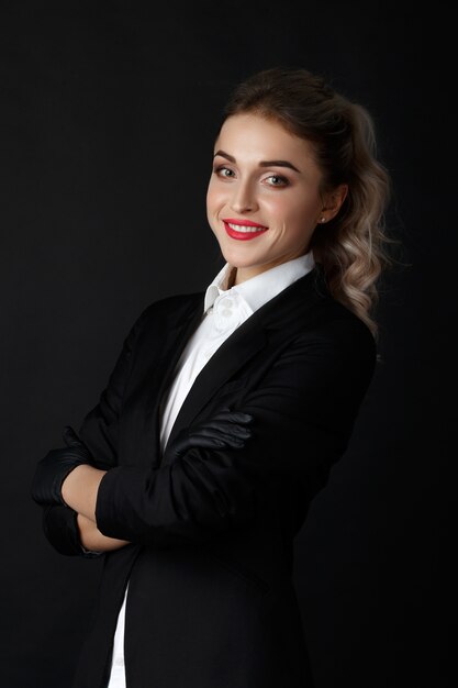 Sexy smart blonde with long curly hair poses in black jacket and black gloves 