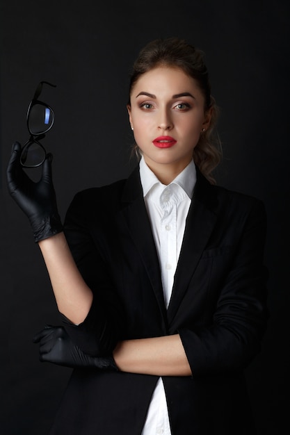 Foto gratuita la bionda intelligente sexy con capelli ricci lunghi posa in giacca nera in uno studio scuro