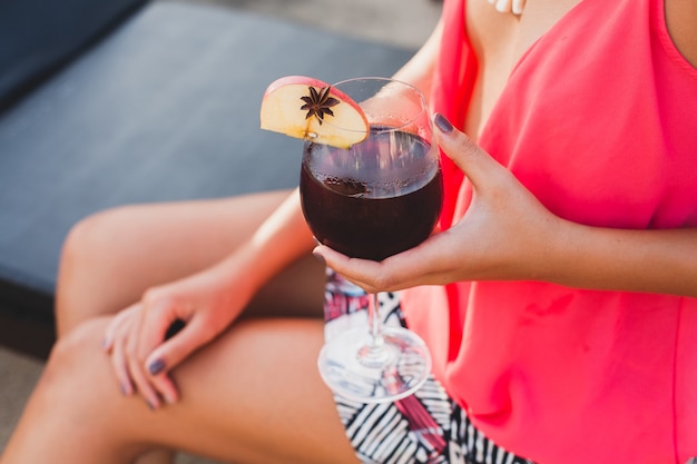 Сексуальная стильная женщина в модном наряде на летних каникулах закрывает руку с бокалом коктейля, развлекаясь в бассейне