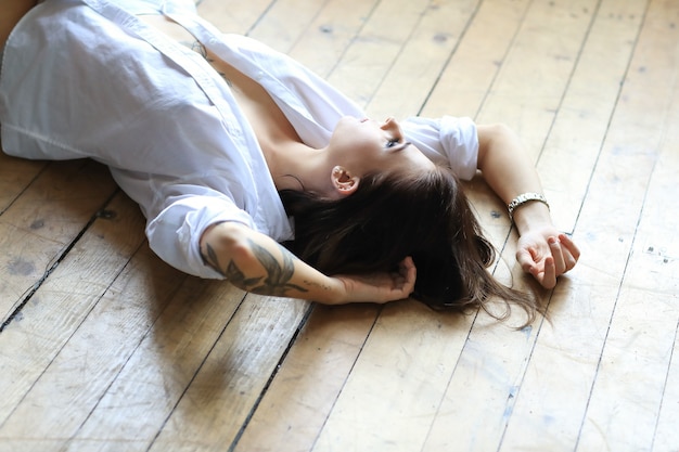 Free photo sexy tattooed woman in a white shirt lying on the wooden floor