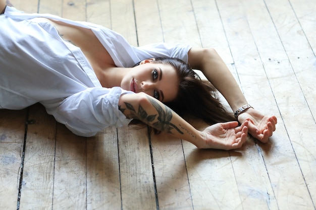 Sexy tattooed woman in a white shirt lying on the wooden floor