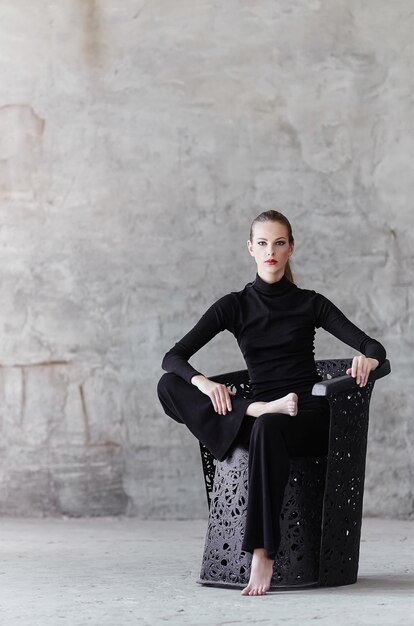 Sexy woman in a black clothes sitting on a chair.