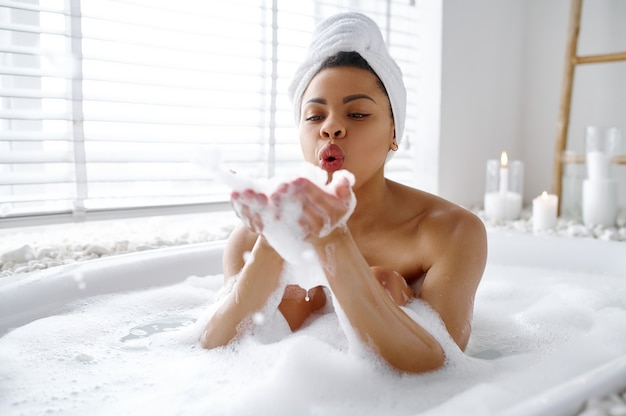 セクシーな女性は泡でお風呂でリラックスします。バスタブの女性、スパの美容とヘルスケア、バスルームのウェルネストリートメント、背景の小石とキャンドル