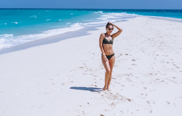 Sexy woman in swim wear standing on sand by the ocean