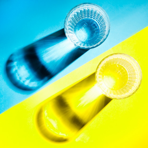 Free photo shadow of clear water glasses on blue and yellow background