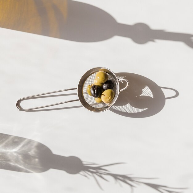 Shadow of strainer with organic olives on white background